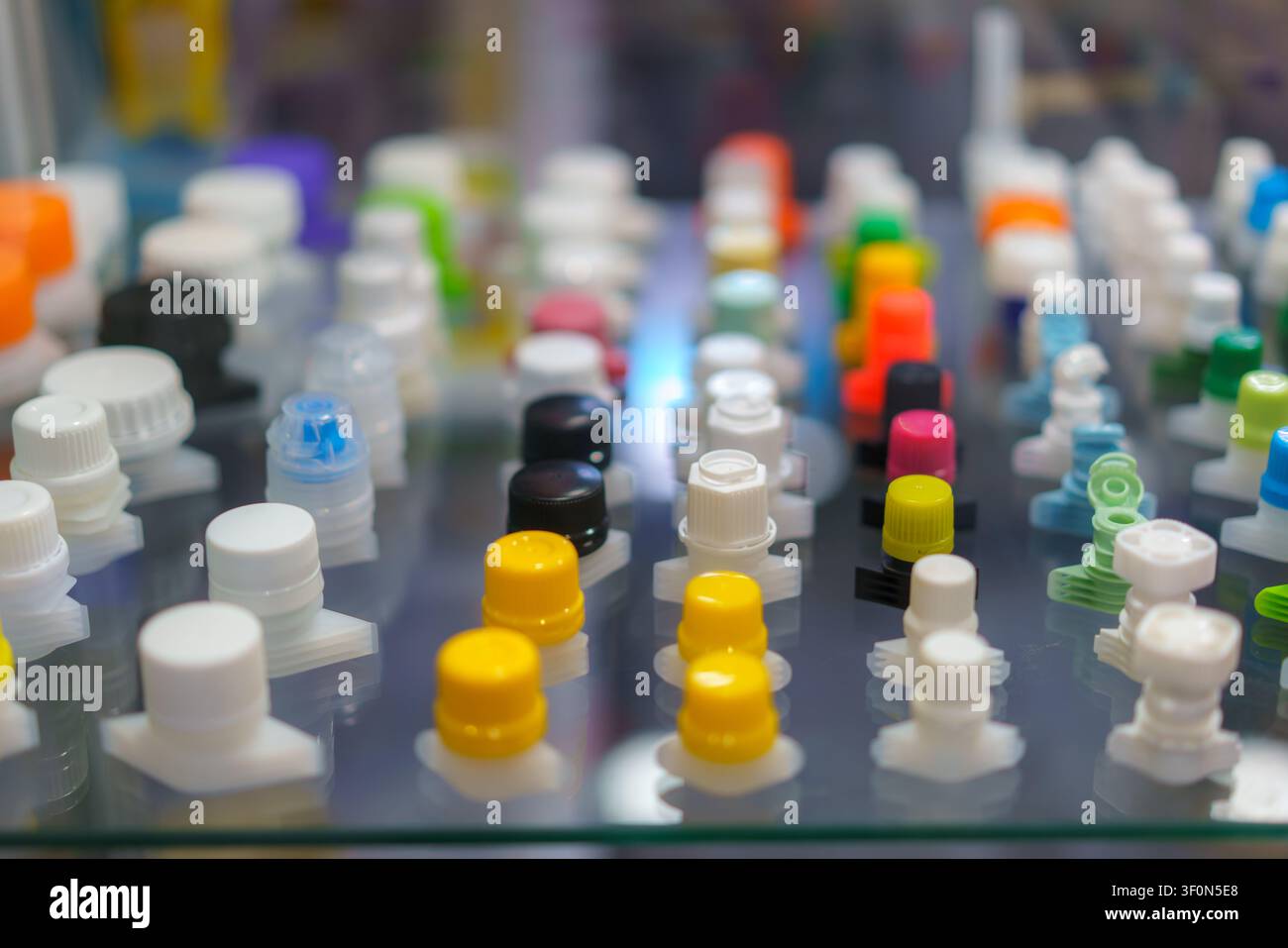 Prima di vari tappi e chiusure colorati in plastica usati per imballaggi flessibili, disposti ordinatamente in file su una mensola di vetro. Foto Stock