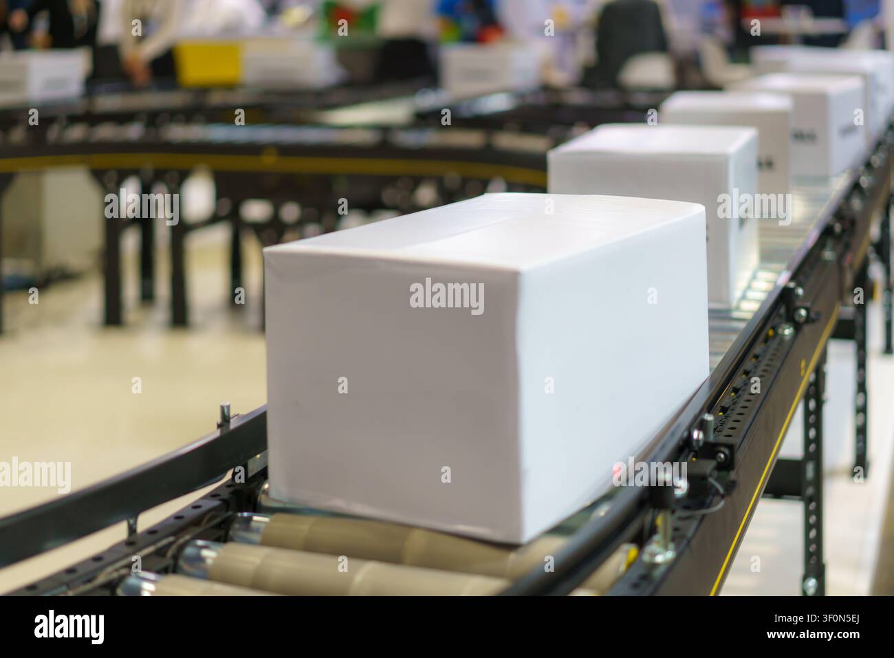 Prima vista di un pacco bianco semplice che viaggia su un sistema di conveyor a rulli in un moderno centro logistico, pronto per la spedizione e la consegna. Foto Stock