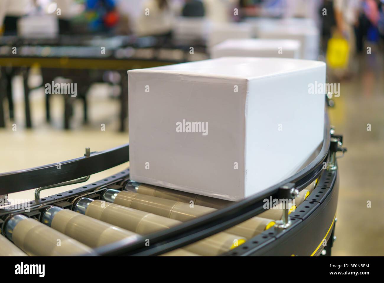 Prima vista di un pacco bianco semplice che viaggia su un sistema di conveyor a rulli in un moderno centro logistico, pronto per la spedizione e la consegna. Foto Stock