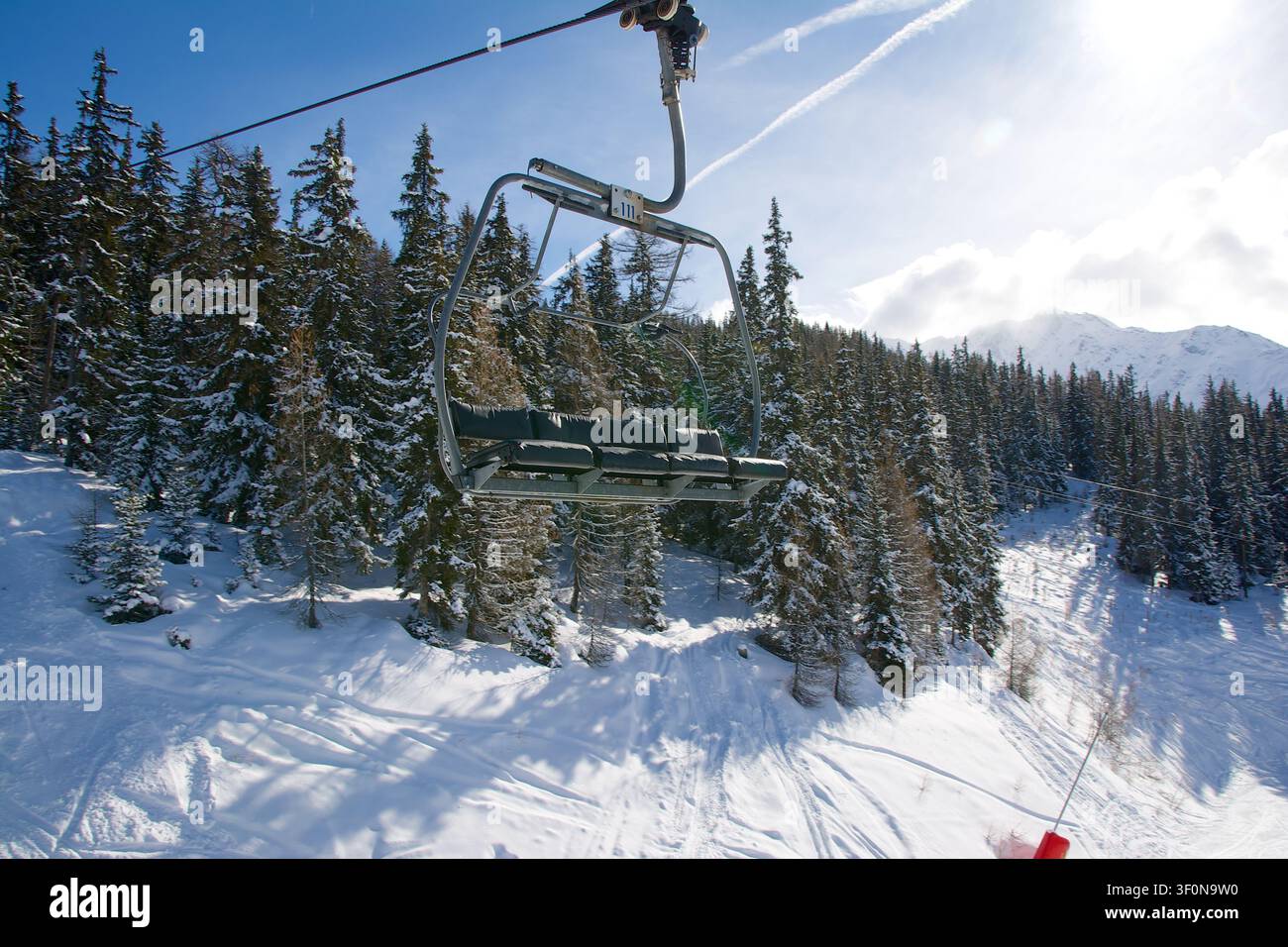 Una seggiovia a quattro posti vuota scivola sopra una pista da sci preparata delimitata da abeti e pini carichi di neve in una stazione sciistica alpina. Foto Stock