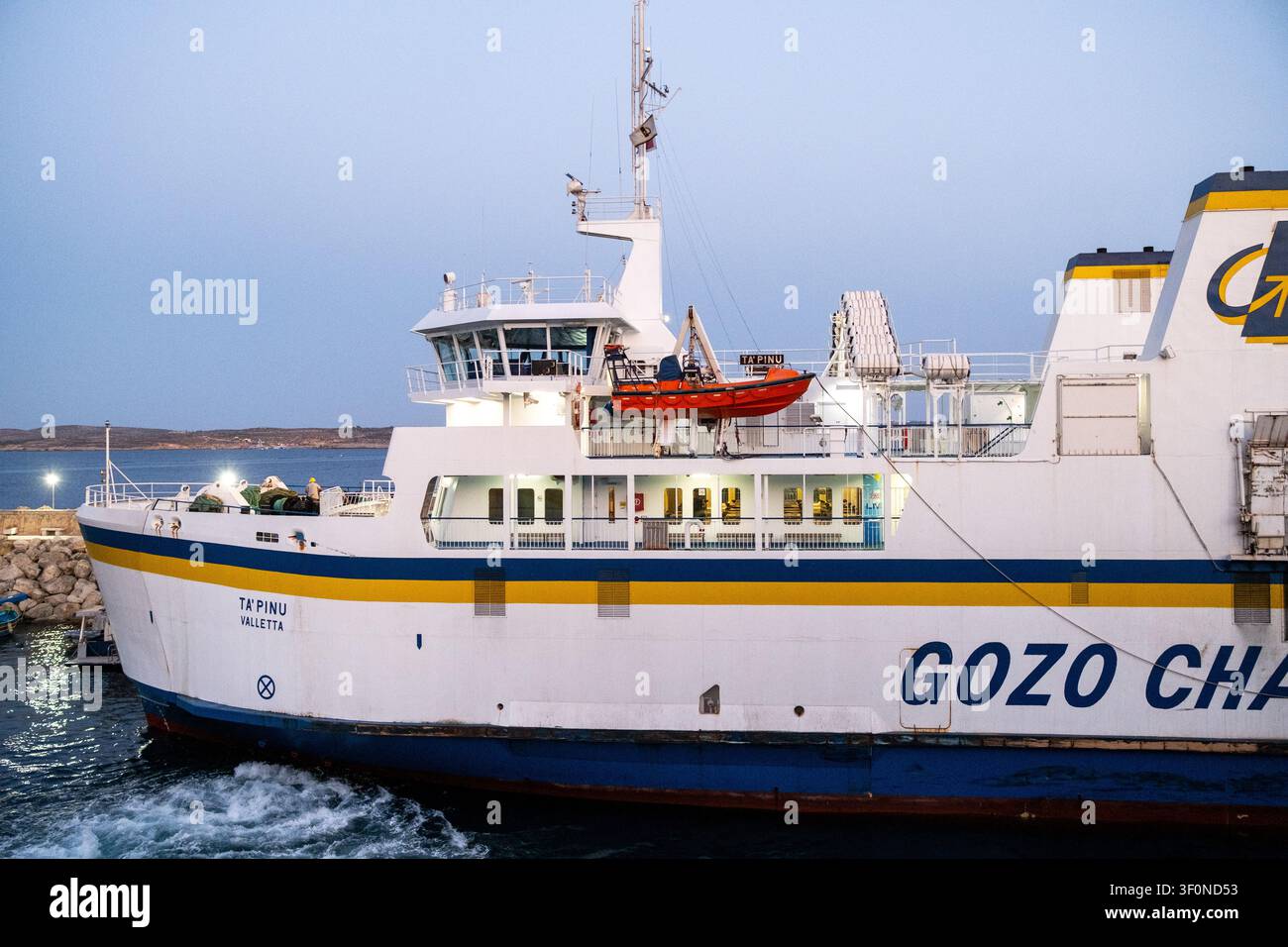 Grande nave passeggeri del Gozo Channel Ta Pinu con visibile branding GOZO CHANNEL, scialuppa arancione, ponte di comando e acqua del mare agitata durante le manovre nel porto Foto Stock
