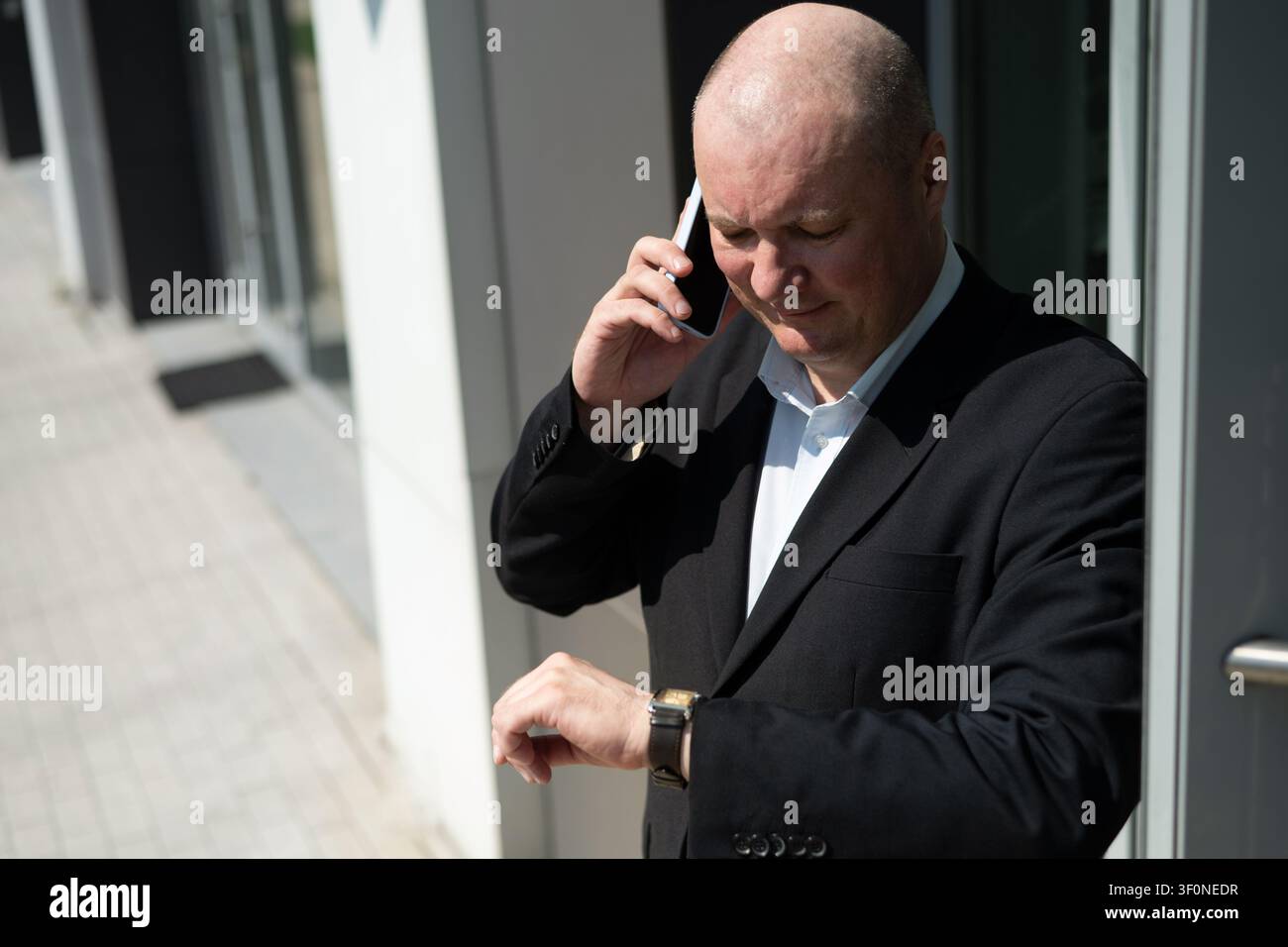 Uomo d'affari caucasico che controlla l'orologio da polso mentre parla al telefono fuori dall'ufficio. Concetto di gestione del tempo, scadenza, programma e chiamata d'affari. Foto Stock
