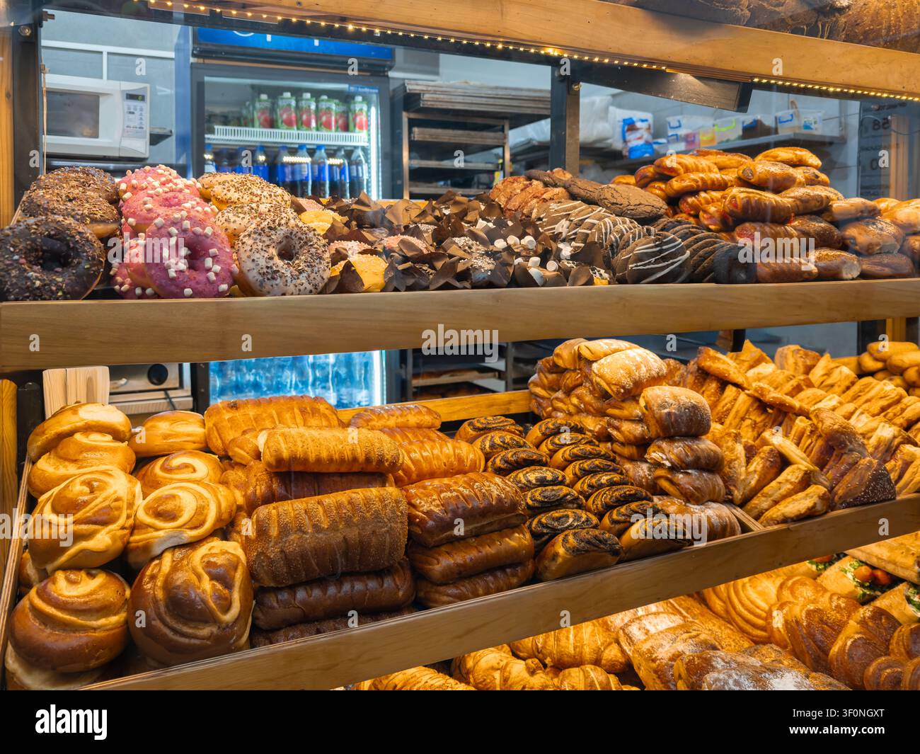 File di pani dorati, panini dolci e ciambelle glassate esposte su scaffali in un negozio di alimentari commerciale, che mostrano deliziose prelibatezze per i clienti Foto Stock