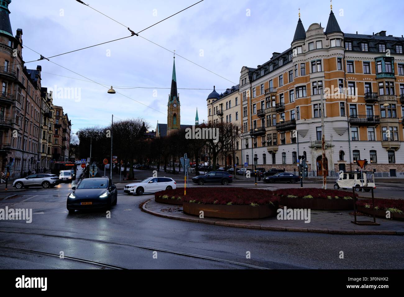 Stockholm, Svezia-28 nov. 2025: Strada di Stoccolma con edifici storici, campanile di una chiesa e auto in movimento. Foto Stock