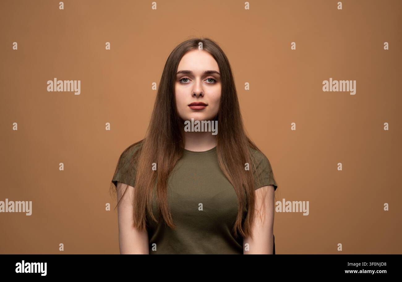 Giovane donna con lunghi capelli castani che posa con sicurezza in un ritratto in studio, incarnando giovinezza, bellezza ed espressione naturale per la pubblicità Foto Stock