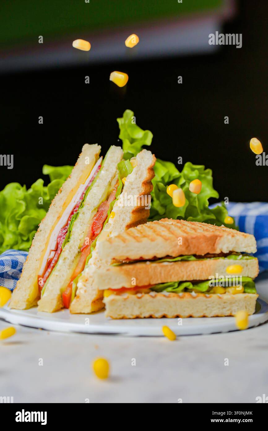 Un piatto contiene panini impilati con strati di carne e verdure. Lattuga verde e pezzi di mais circondano il piatto. La luce cade sul cibo a pran Foto Stock