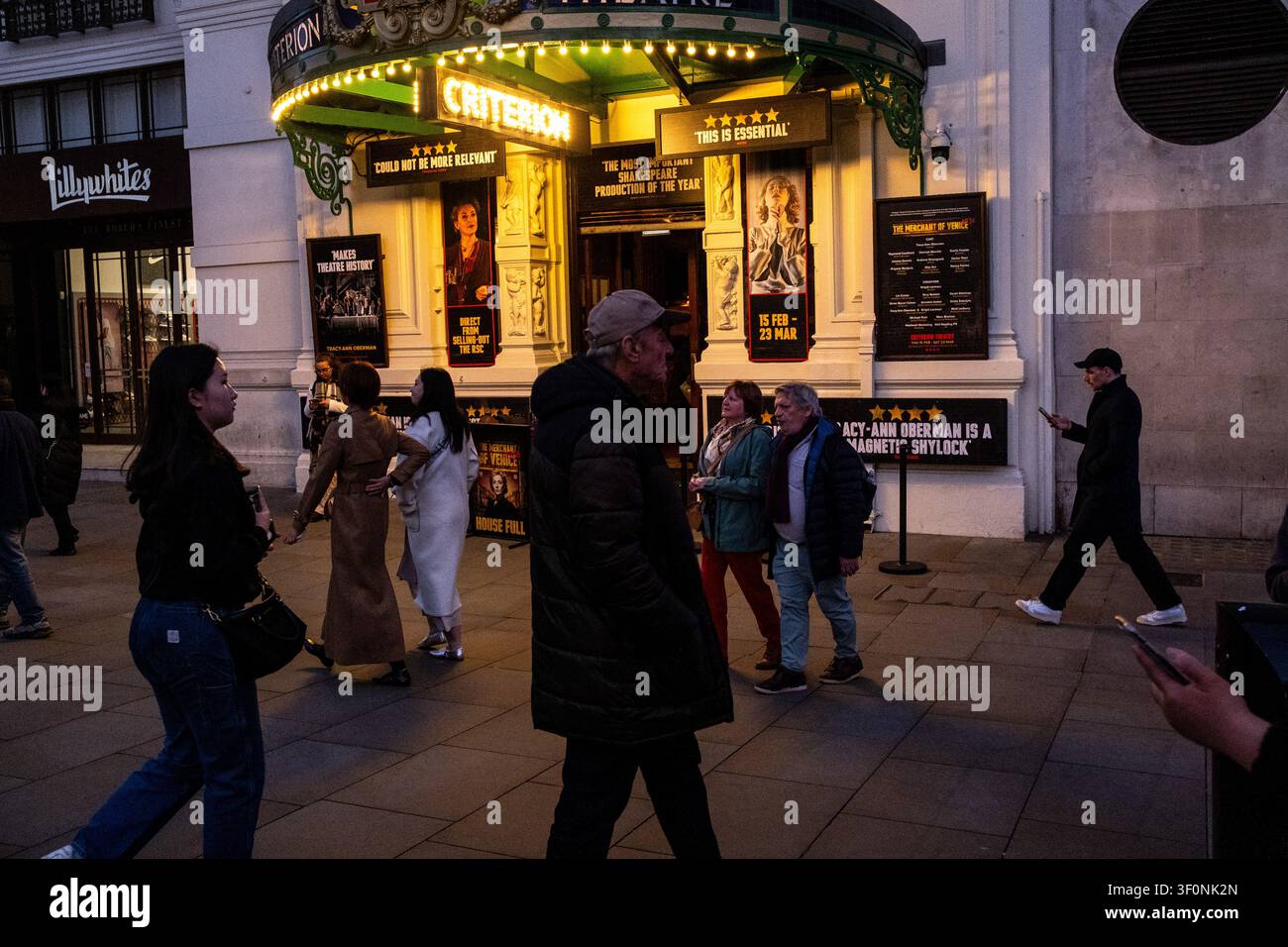 I pedoni passano davanti all'ingresso illuminato del Criterion Theatre, con poster che pubblicizzano Il Mercante di Venezia 1936 interpretato da Tracy Ann Oberman Foto Stock