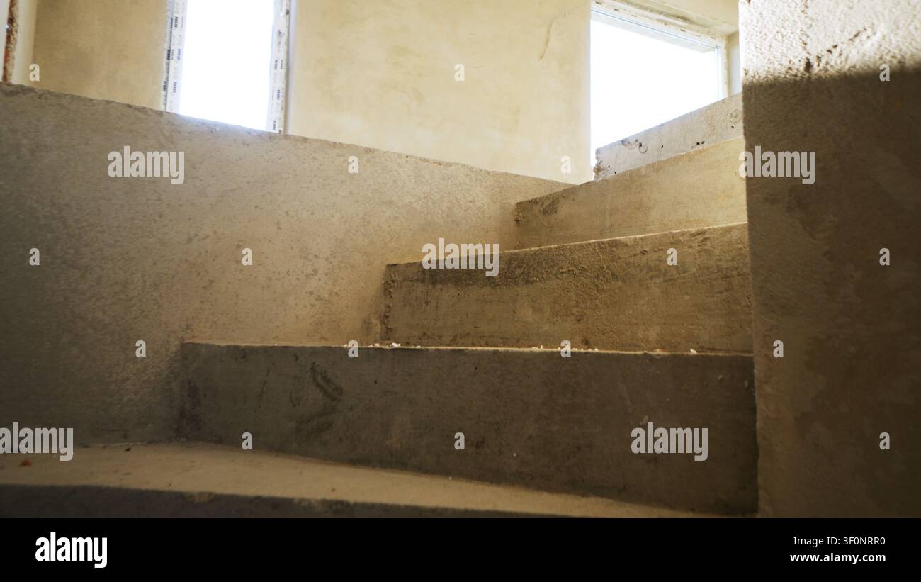 Scalini in cemento all'interno di una casa incompiuta, che mostrano i progressi dell'edificazione in un interno crudo e vuoto con luce naturale Foto Stock