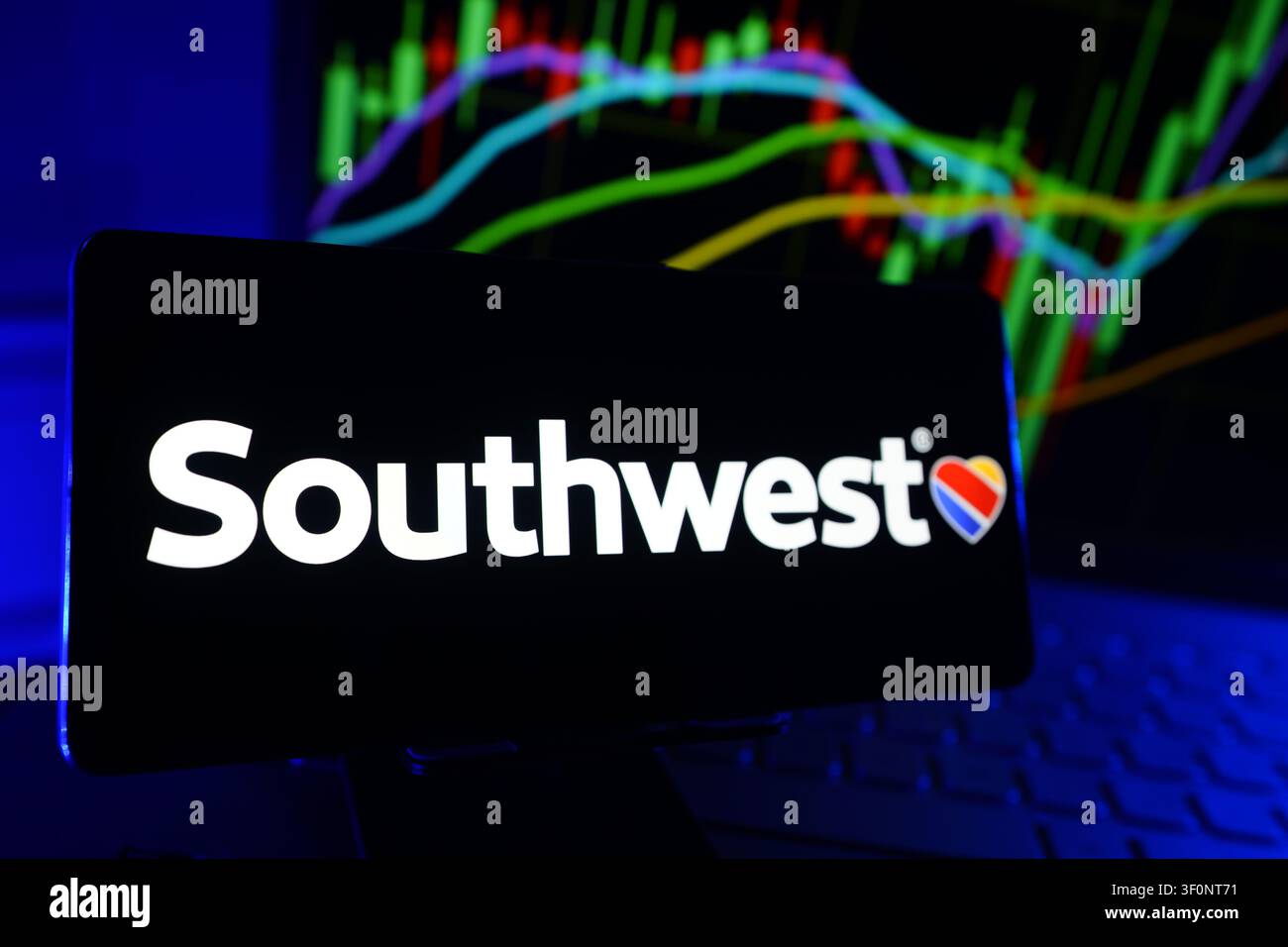 Logo di Southwest Airlines Co visualizzato su uno schermo smartphone davanti a un computer che mostra grafici di performance finanziarie del mercato azionario Foto Stock