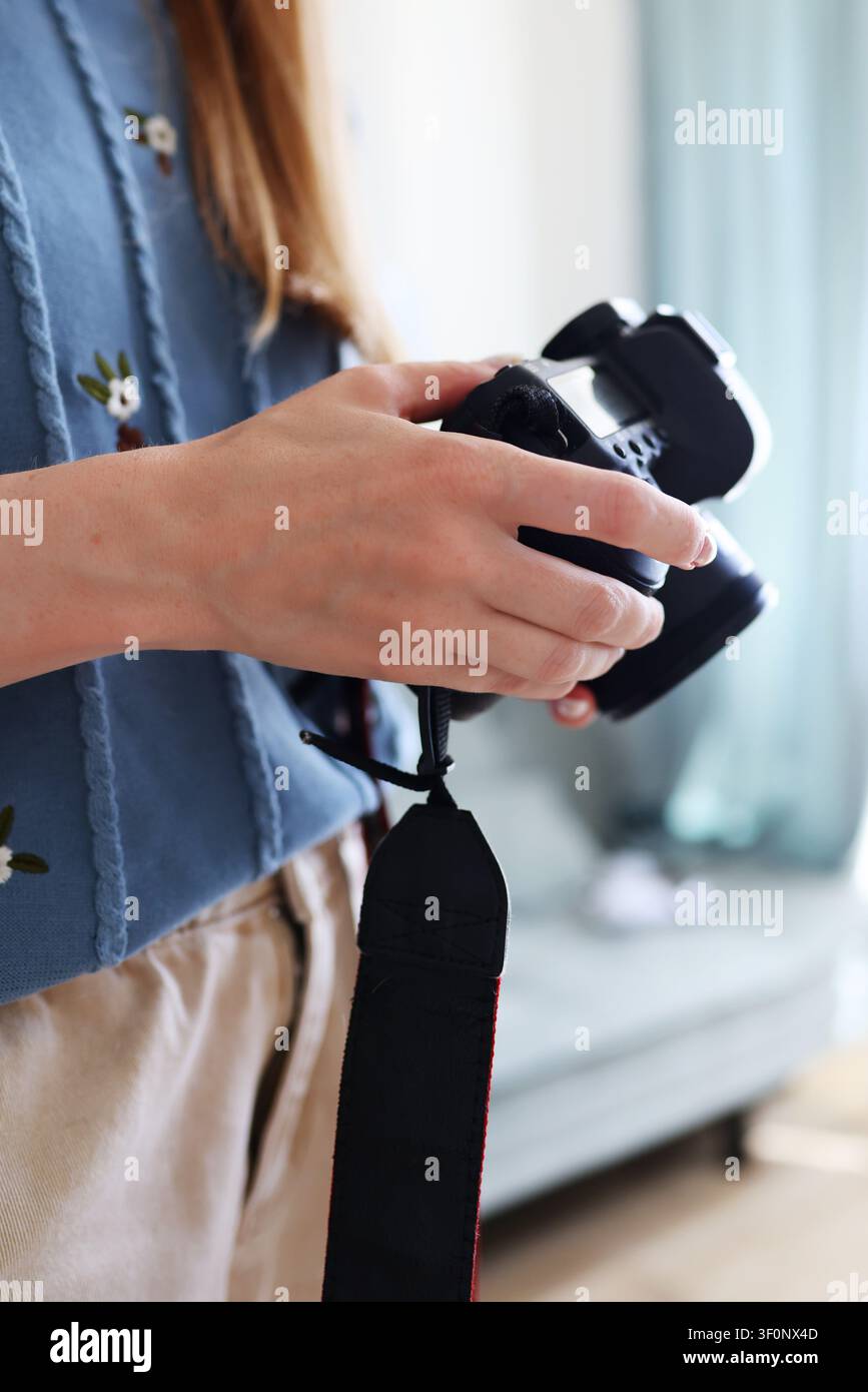 Primo piano di una donna che tiene una fotocamera senza mirror e regola le impostazioni, attrezzatura fotografica e concetto di stile di vita creativo. Foto Stock