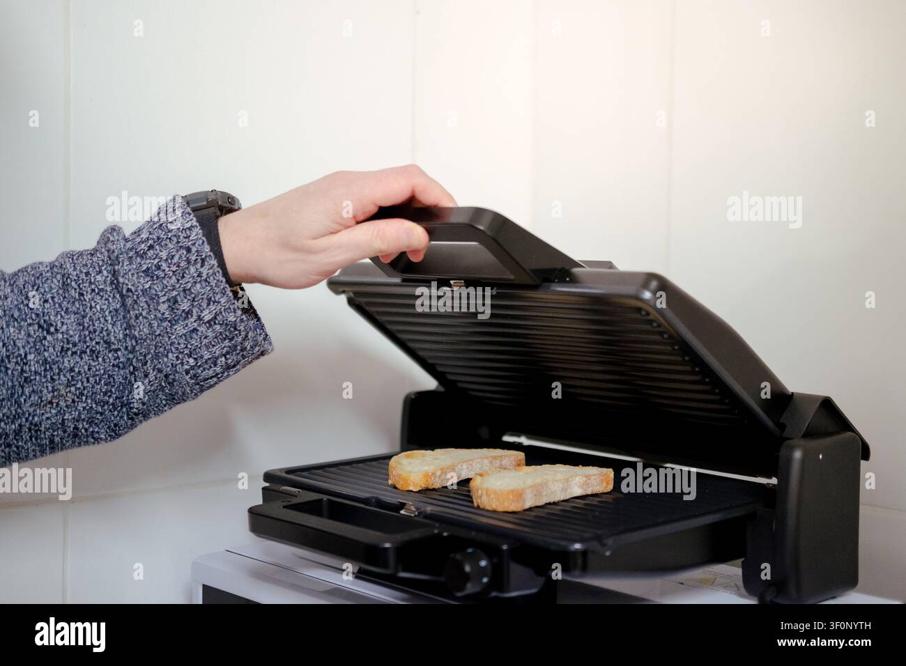 Mano che apre una griglia a contatto con due fette di pane che si grigliano Foto Stock