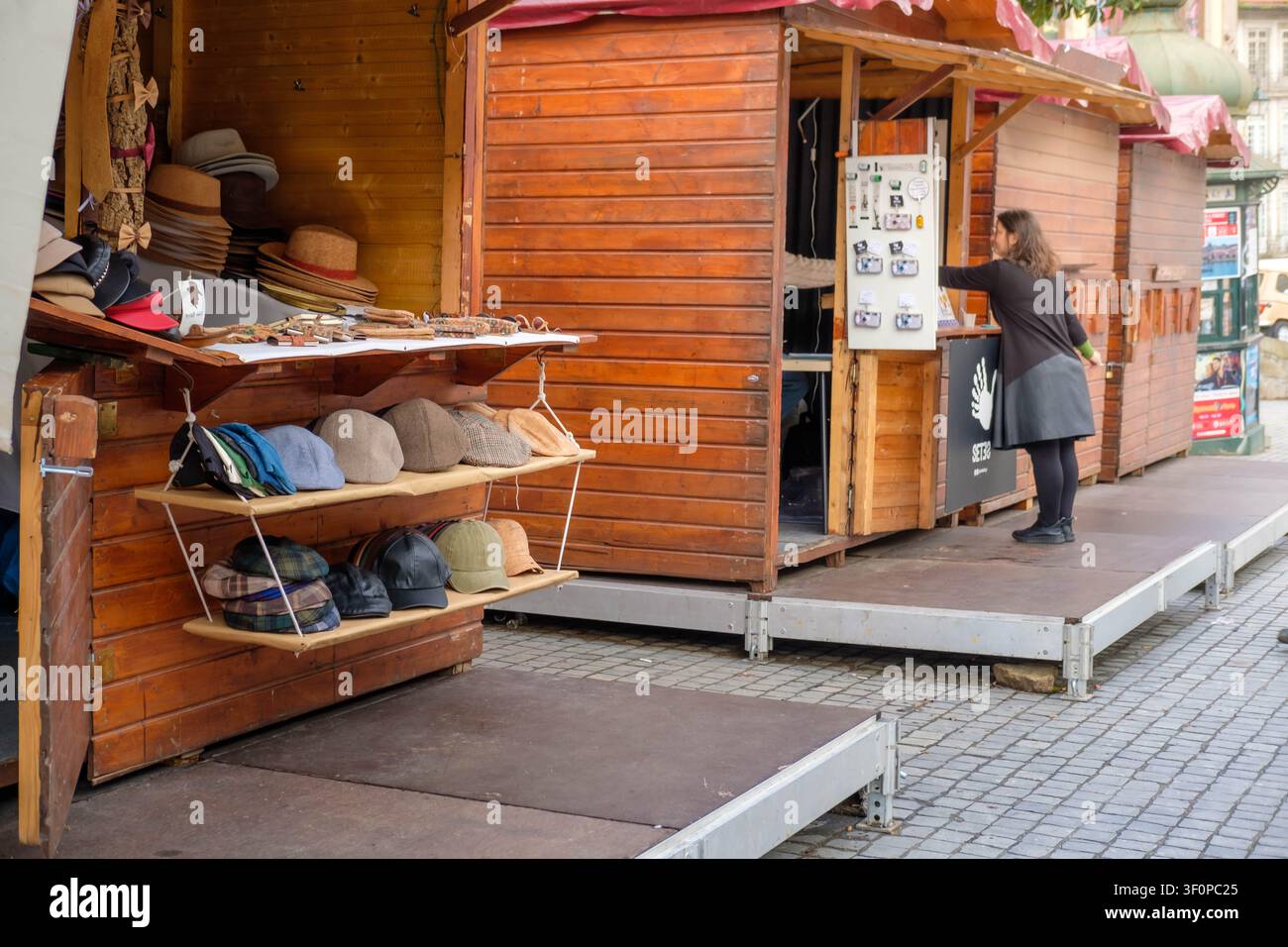 Oporto, 29 novembre 2024: Donna in piedi dietro un banco del mercato in legno con vari cappelli in esposizione. Foto Stock