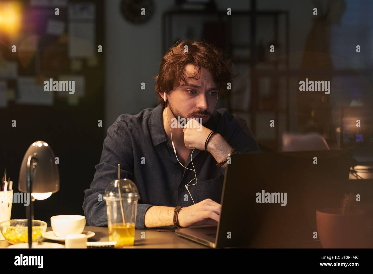 Uomo adulto che lavora fino a tardi su un laptop durante un turno serale remoto Foto Stock