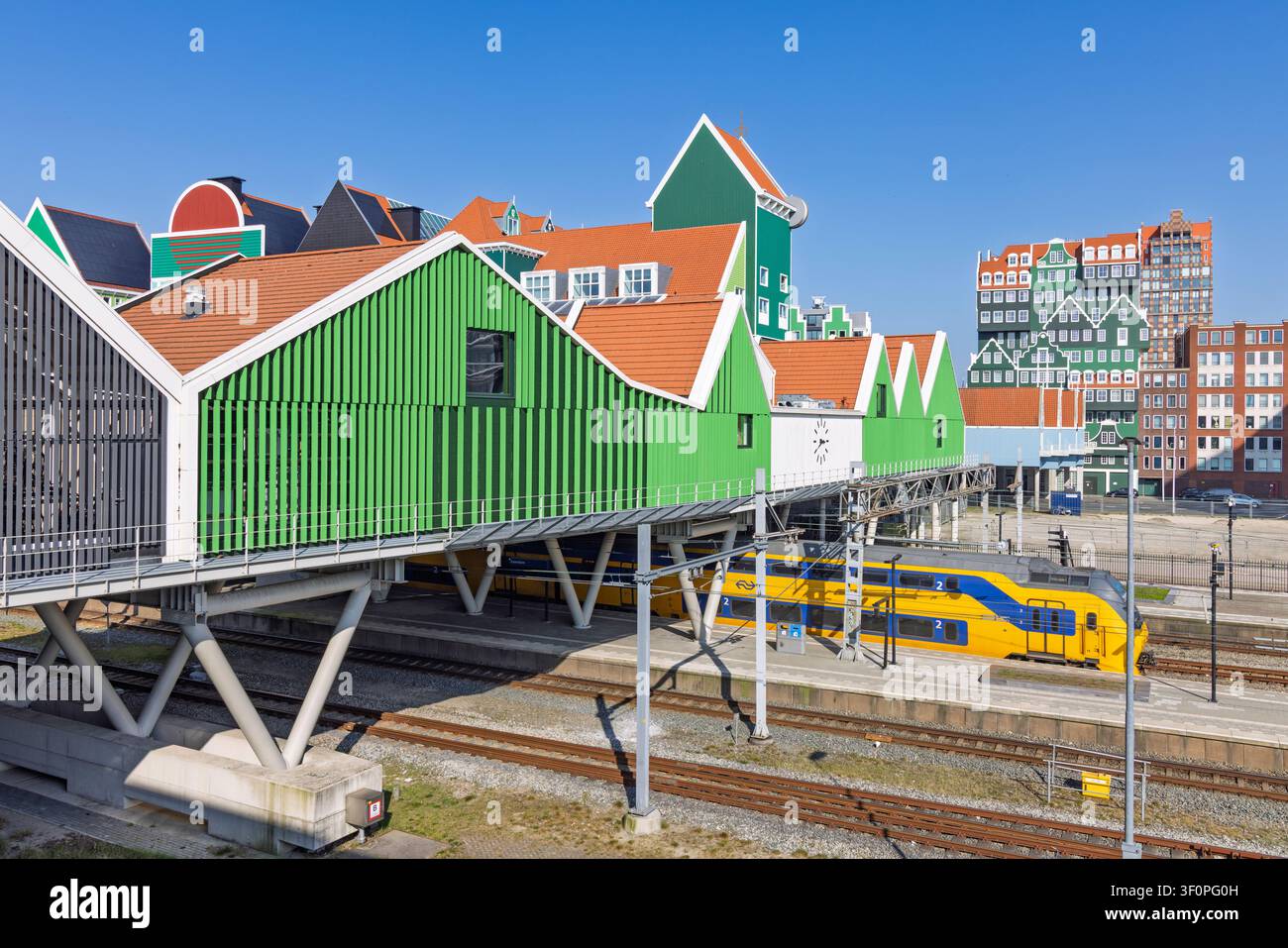 Zaandam, Paesi Bassi, 22 marzo 2026. L'architettura unica e famosa delle case impilate della stazione ferroviaria di Zaandam con un treno giallo NS al binario Foto Stock