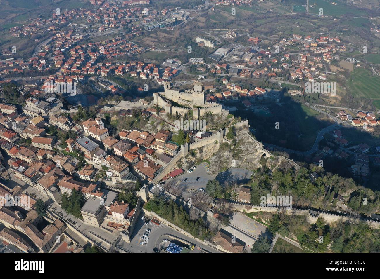 Vista aerea della storica fortezza di Guaita Tower sul Monte Titano, circondata da mura in pietra, tetti in terracotta e il paesaggio urbano di San Mari Foto Stock