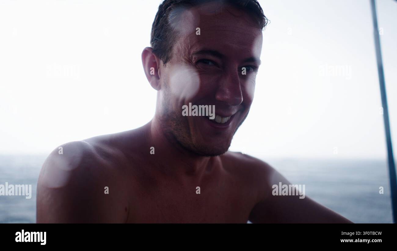 Uomo allegro che sorride, assaporando una giornata estiva rinfrescante sull'acqua Foto Stock