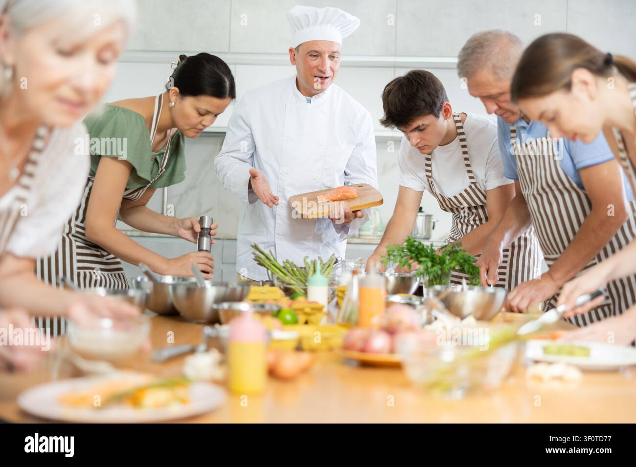 Chef maschio esperto che insegna a cucinare il salmone durante una lezione di cucina di gruppo Foto Stock