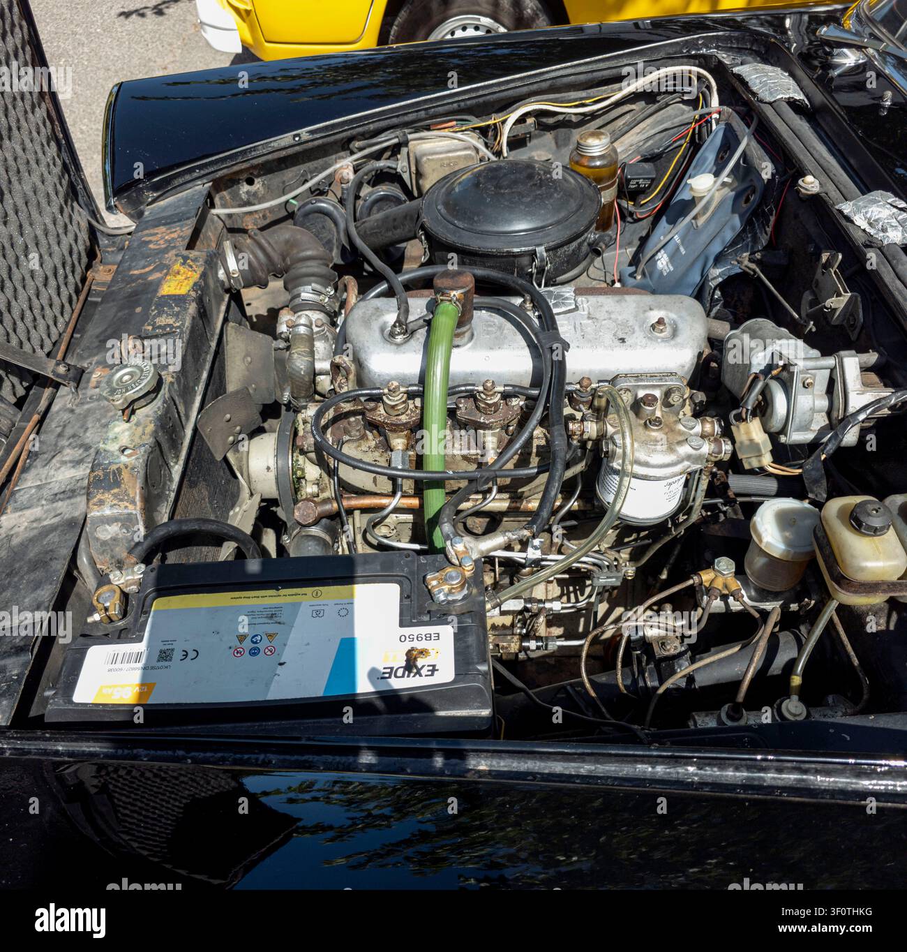 TAVERNES BLANQUES, SPAGNA - 14 GIUGNO 2026.Sotto il cofano, un'auto classica mostra il vano del motore a combustione interna con una batteria Exide. L'ambientazione è Foto Stock