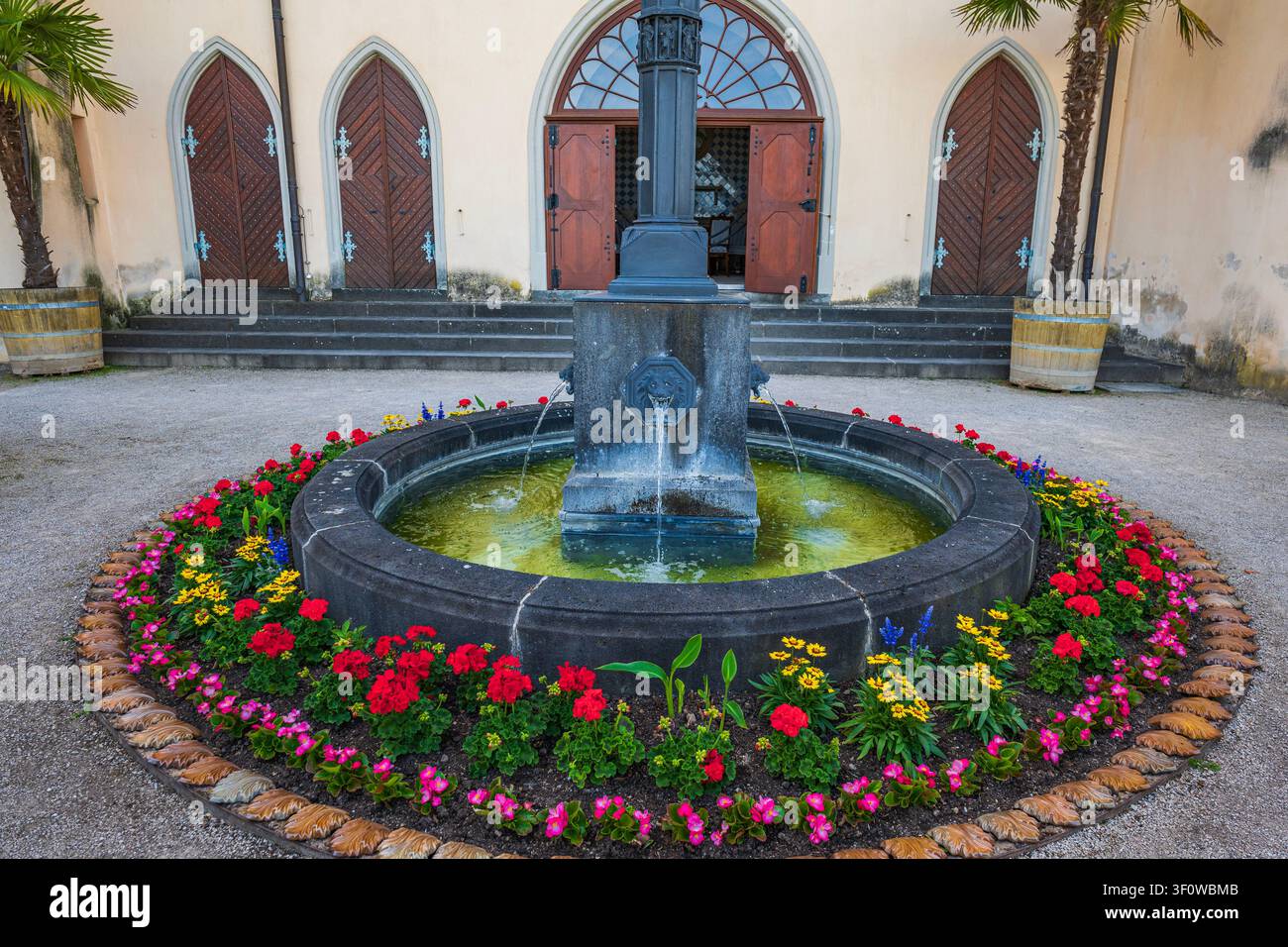 Fontana in pietra con aiuola fiorita nel cortile del castello di Stolzenfels con porte ad arco in legno e palme in vaso in Germania Foto Stock