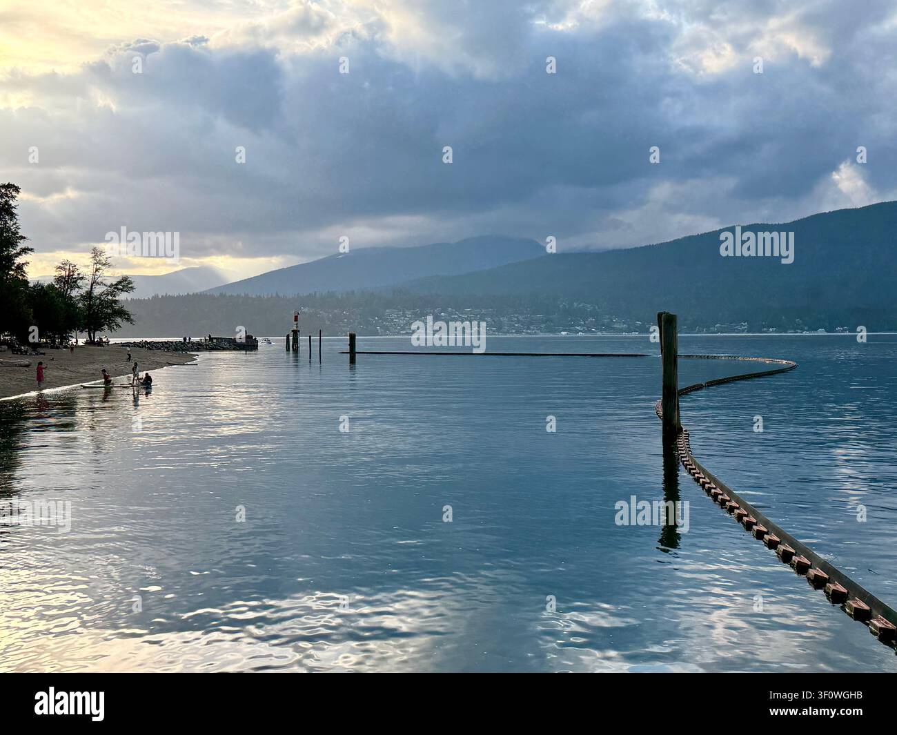 Vista suggestiva della sera sul Burrard Inlet dal Barnet Marine Park a Burnaby, Metro Vancouver, con nuotatori vicino alla riva e montagne in lontananza. - Immagine stock catturata con smartphone
