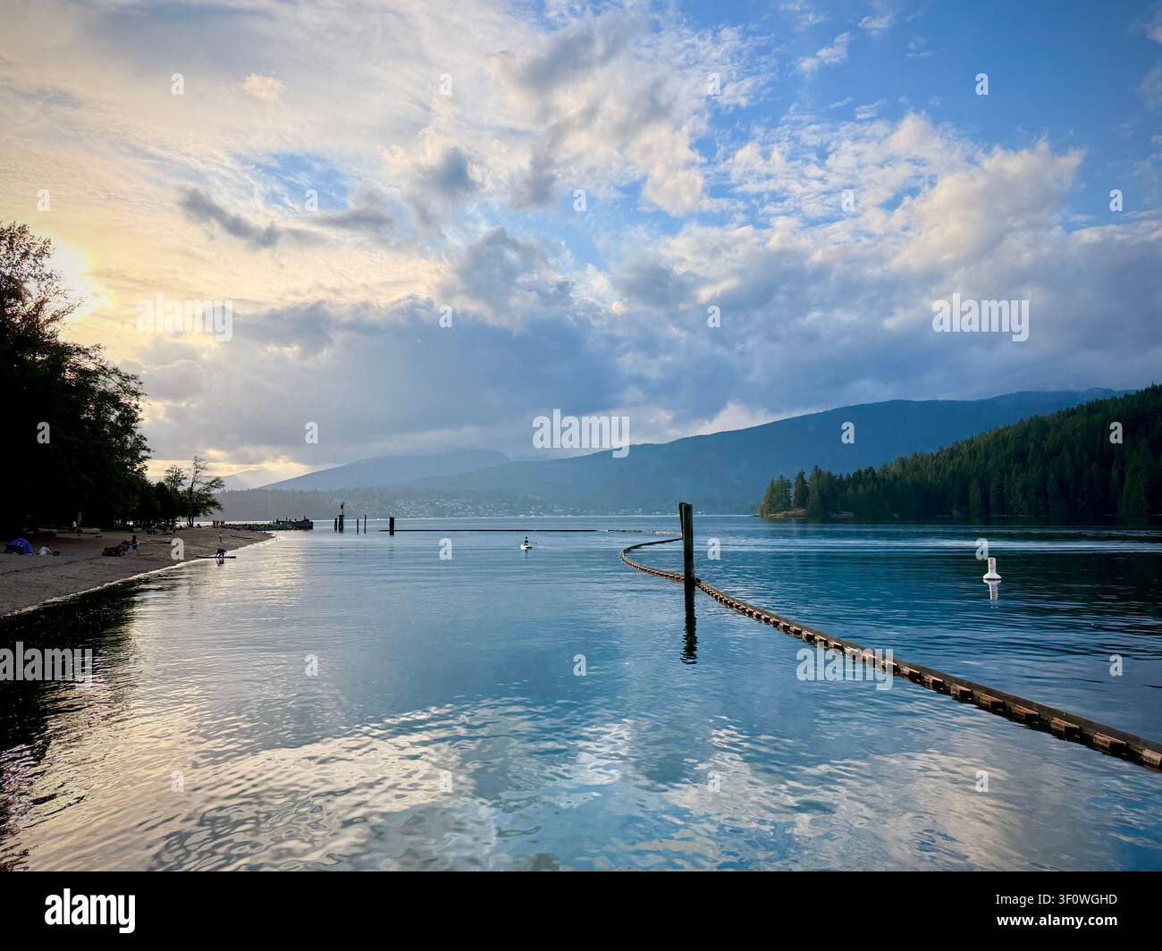 Vista suggestiva della sera sul Burrard Inlet dal Barnet Marine Park a Burnaby, Metro Vancouver, con nuotatori vicino alla riva e montagne in lontananza. Foto Stock