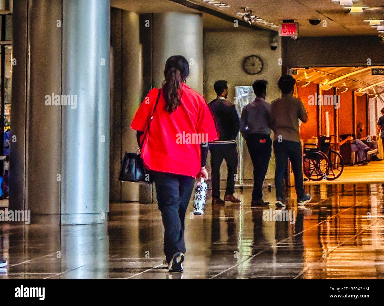 Una donna con un cappotto rosso segue altre persone lungo un corridoio Foto Stock