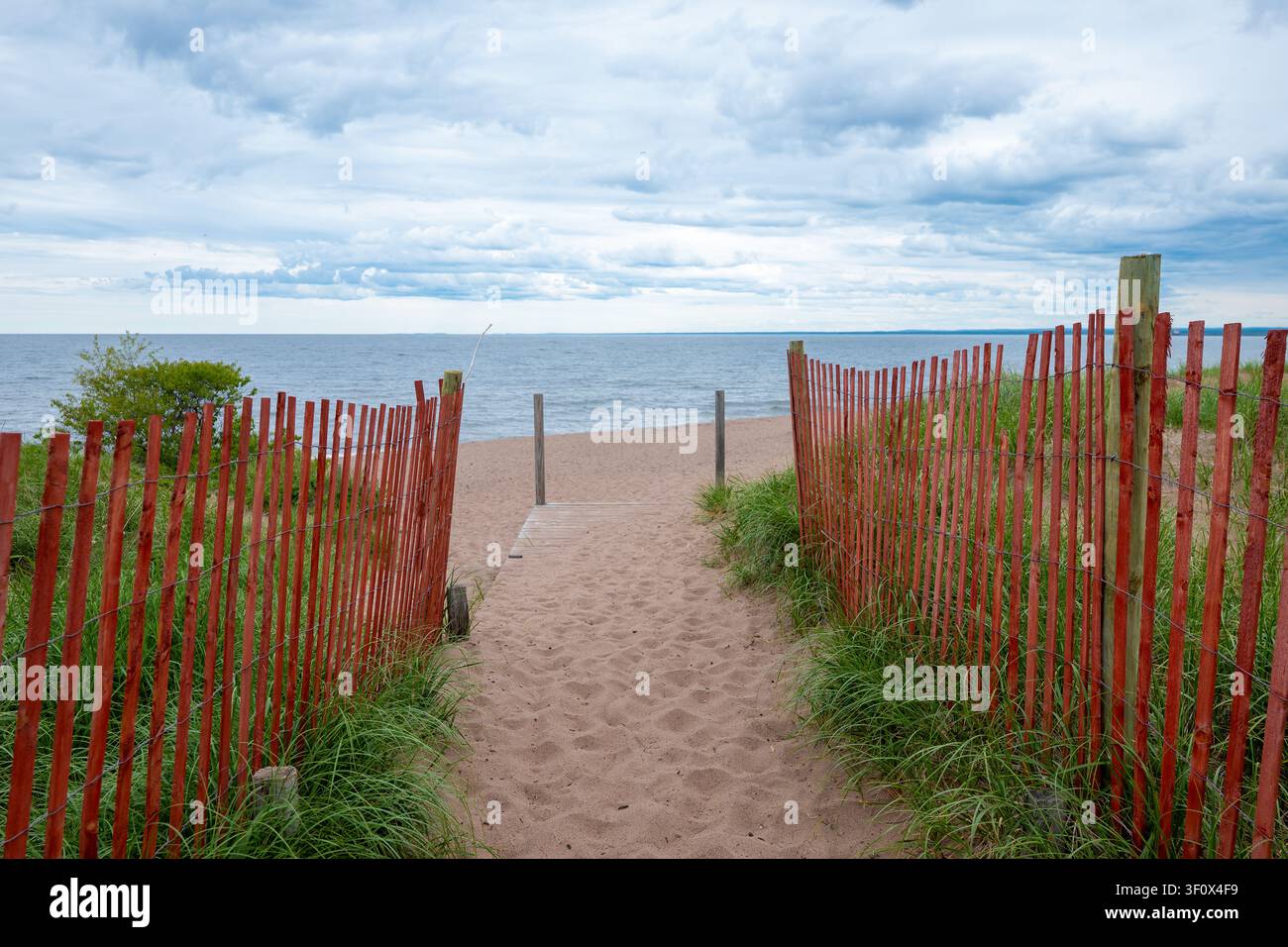 Percorso di accesso a una spiaggia sabbiosa fiancheggiato da recinzione rossa per la neve e erba delle dune che conduce alla riva del Lago Superiore a Park Point, Duluth, Minnesota in una giornata nuvolosa su Foto Stock