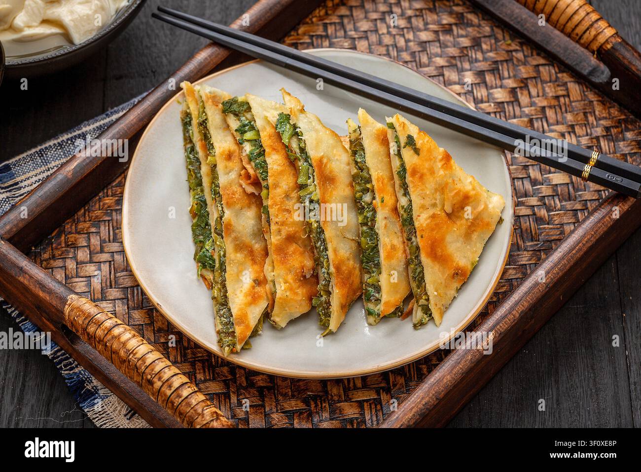 Taschetti di erbe aromatiche cinesi fritti tagliati a triangoli su piatto di ceramica nera, tortini alle erbe saporiti Foto Stock