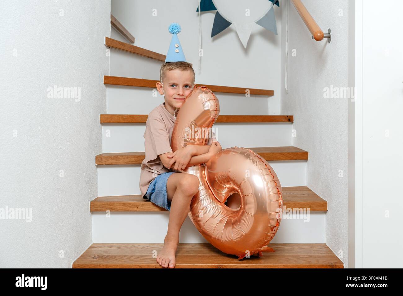 Un bambino gioioso si siede su una scala adornata con un palloncino colorato, circondato da un'atmosfera calda e festosa. La scena cattura una famiglia felice Foto Stock