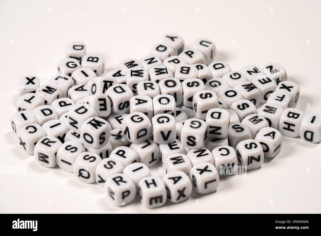 Piccole perle bianche con lettere nere sono sparse su una superficie chiara, ideali per progetti di artigianato, giochi o attività educative che coinvolgono sp Foto Stock