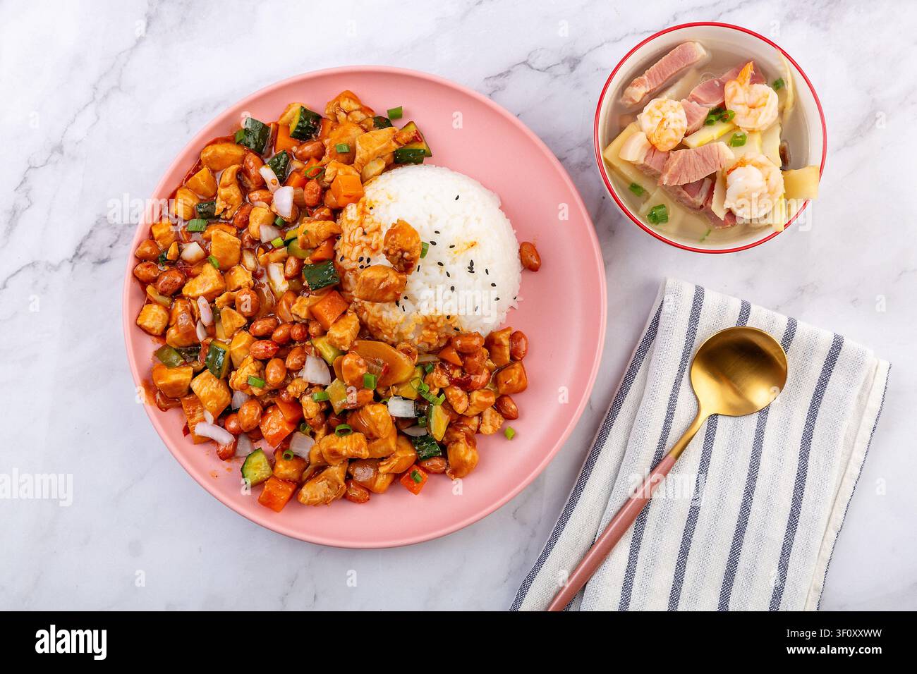 Pollo Kung Pao cinese piccante con arachidi e verdure servito su riso bianco in un piatto rosa. Foto Stock
