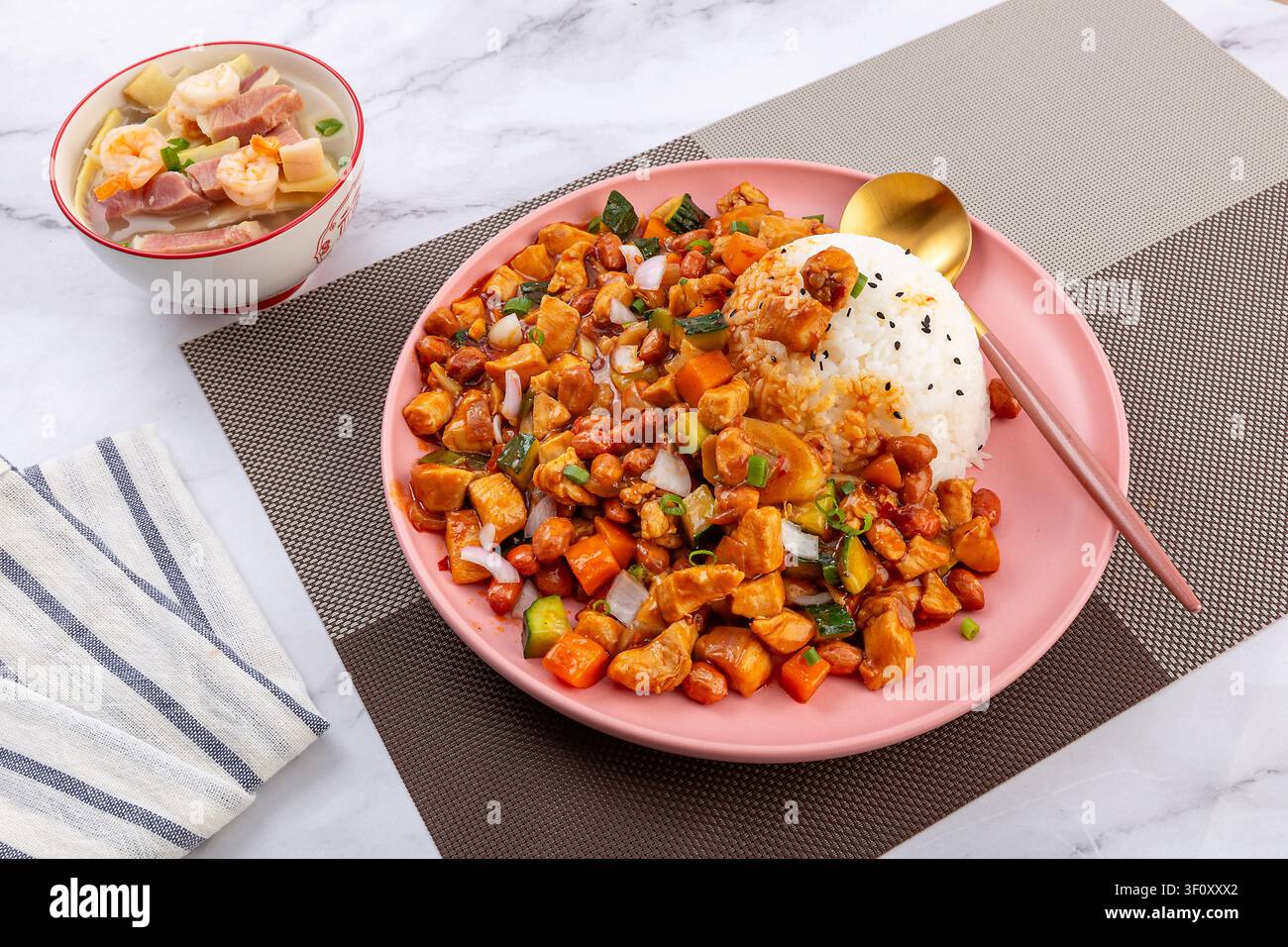 Pollo Kung Pao cinese piccante con arachidi e verdure servito su riso bianco in un piatto rosa. Foto Stock