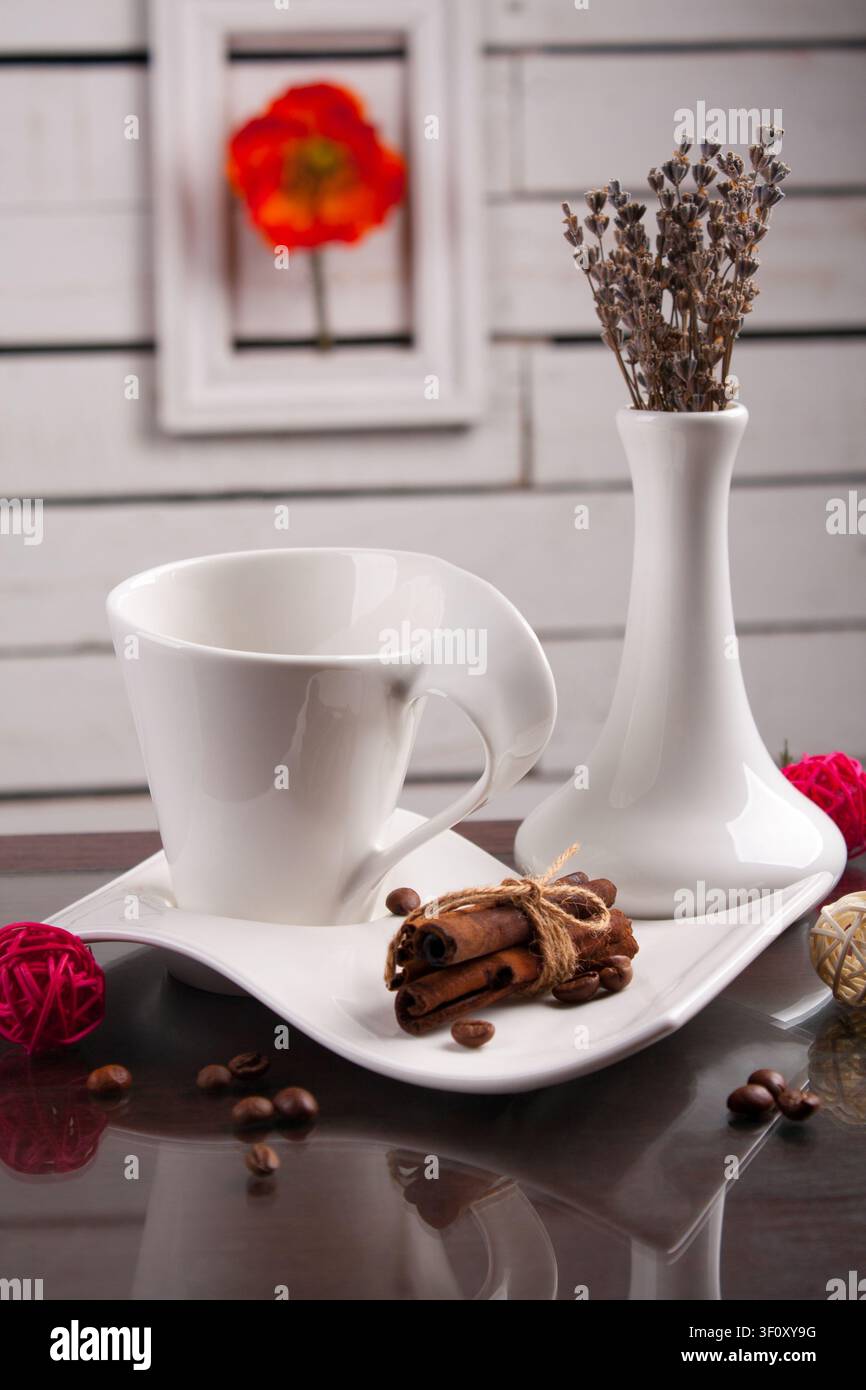 Tazza da caffè bianca elegante con vaso decorativo, fiori secchi e spezie disposti in una composizione di natura morta luminosa. Concetto di atmosfera accogliente a casa, Foto Stock