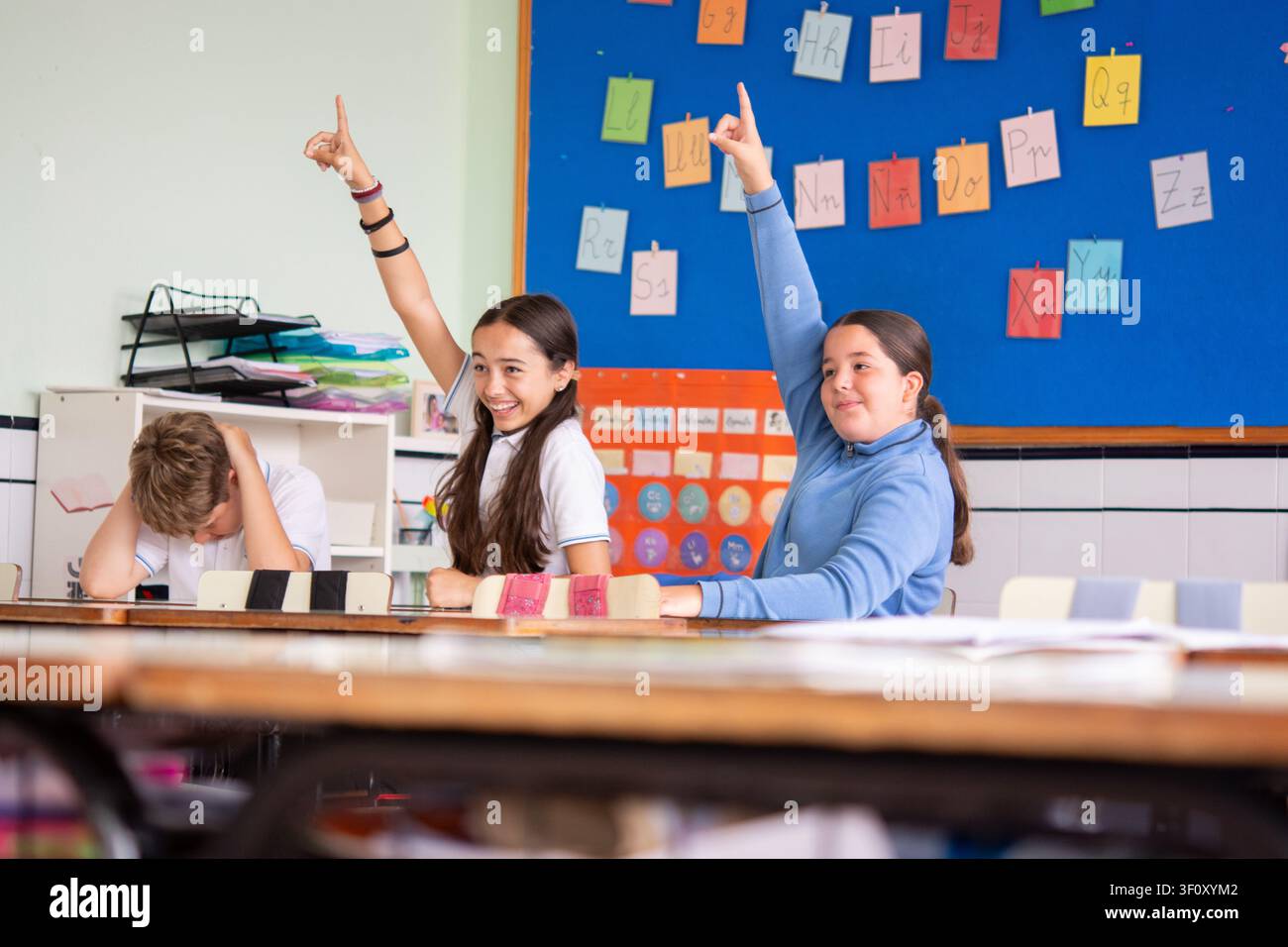 Alunni delle scuole elementari che alzano le mani durante una lezione in classe. Foto Stock