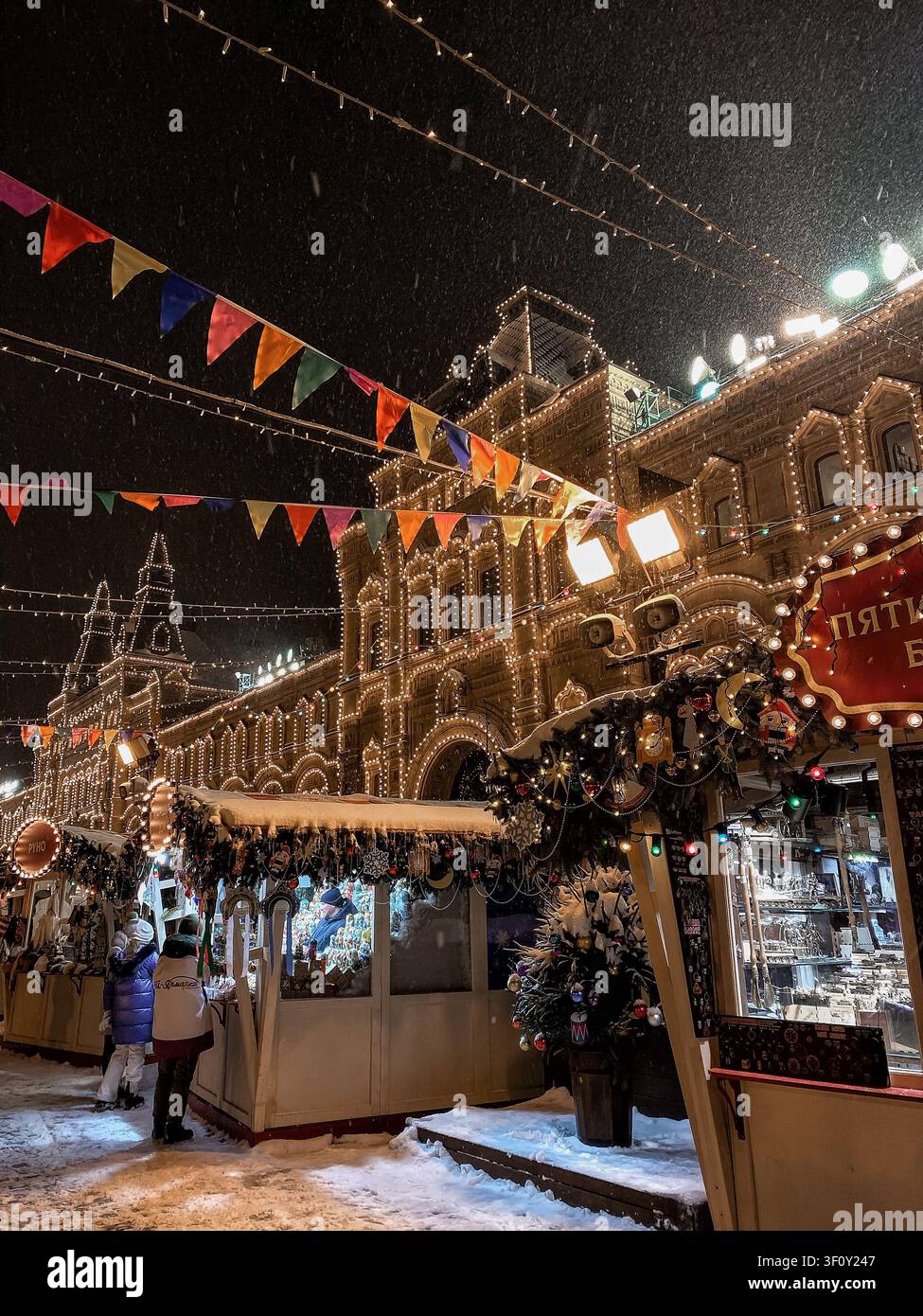Mosca, Russia - 22 gennaio 2022: Bancarelle del mercato natalizio innevate accanto a un edificio storico illuminato di notte - Immagine stock catturata con smartphone