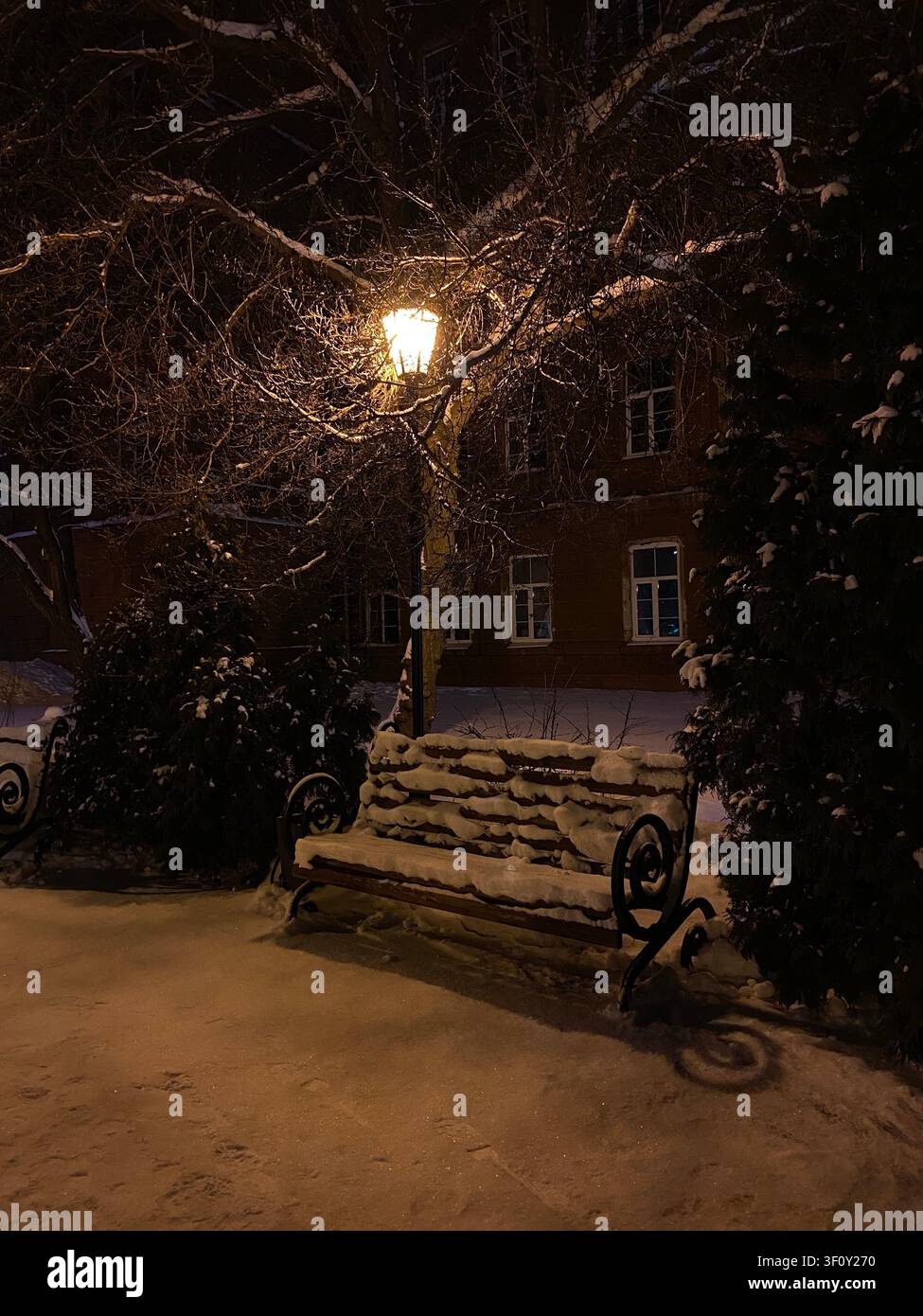 Panchina del parco coperta di neve sotto un caldo lampione in una notte d'inverno panchina invernale, panchina innevata, panchina del parco, panchina vuota, inverno - Immagine stock catturata con smartphone