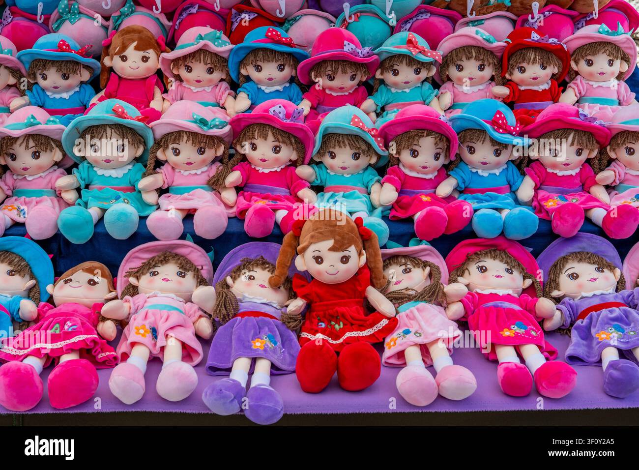 Sineu, Spagna, 22 aprile 2026: File vivaci di bambole di peluche morbide in abiti colorati, ordinate su uno stand di mercato, con una singola bambola rossa al centro Foto Stock