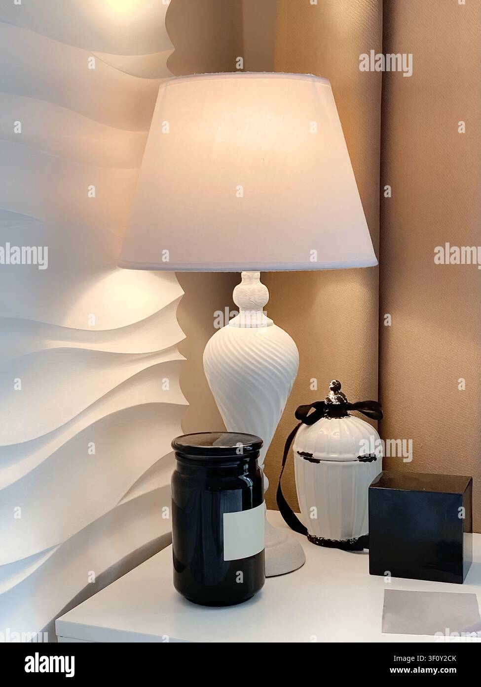 Stile elegante per il comodino con una classica lampada bianca, una candela profumata, una scatola di profumi e un barattolo decorativo in un interno caldo e minimalista. Foto Stock
