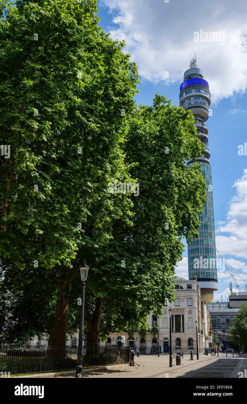 Londra - 07 14 2022: Vista della torre BT da Fitzroy Square incorniciata da alberi e recinzioni. Piazza urbana con grandi alberi a foglia nel primo piano, recinzioni in ferro Foto Stock