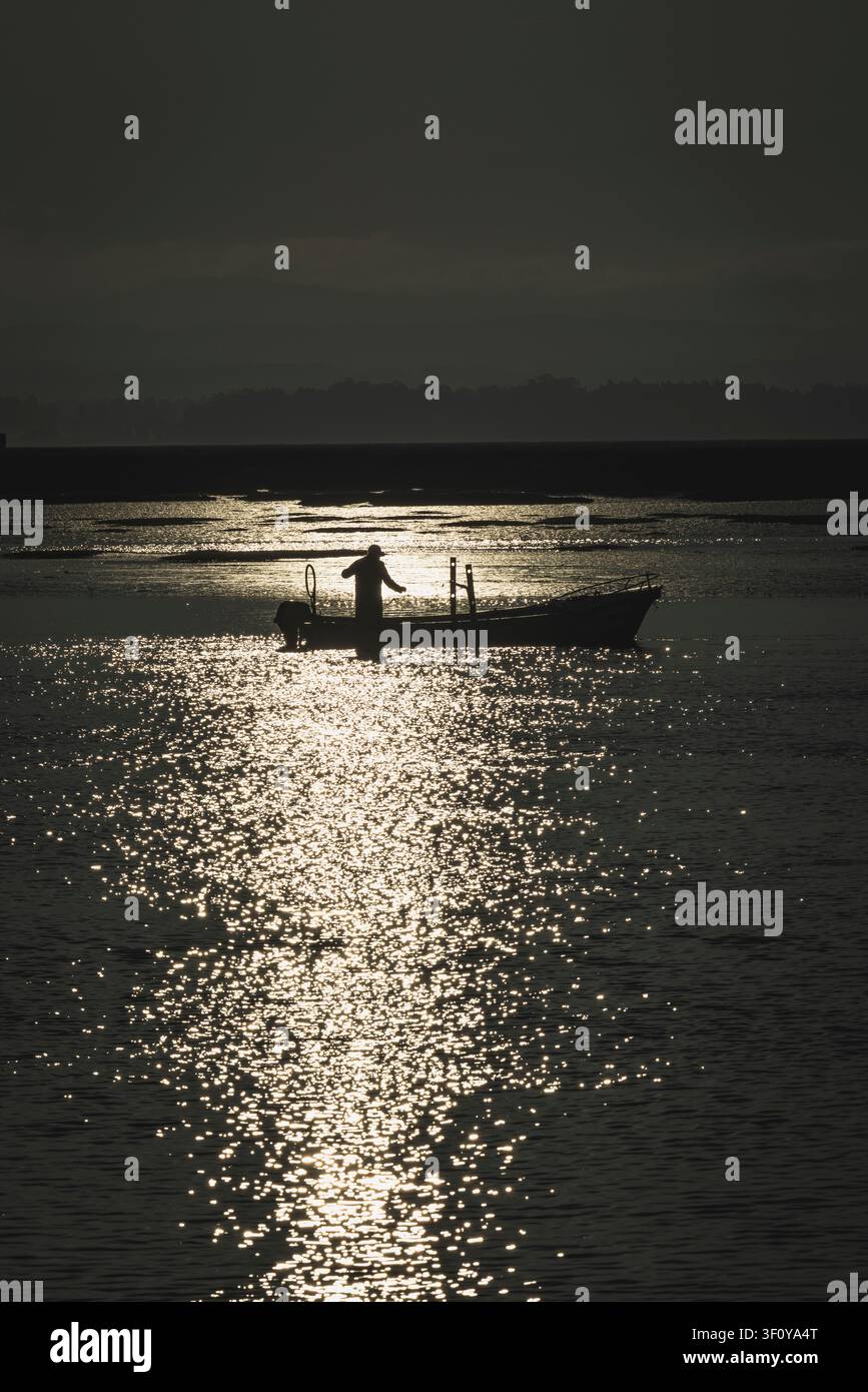 Pescatore in controluce su una barca nell'acqua scintillante Foto Stock