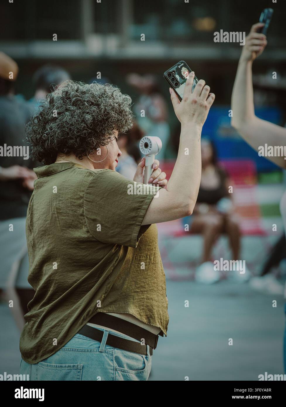 Donna con ventaglio portatile che filma con il suo telefono Foto Stock