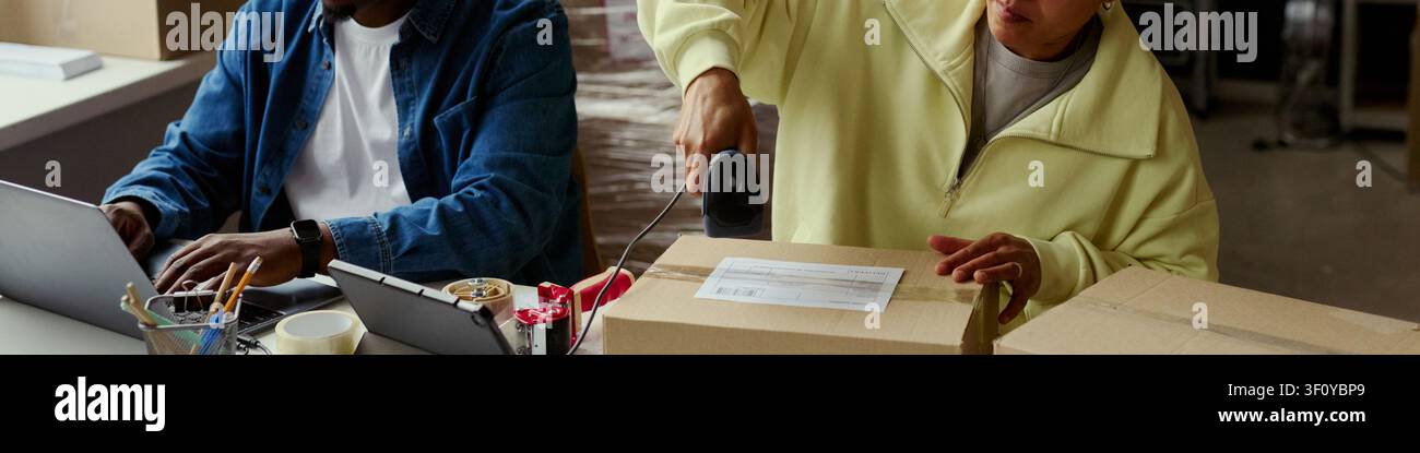 Intestazione di colleghi adulti che elaborano un ordine di spedizione, scansionano un codice a barre su un pacco mentre lavorano con laptop e tablet in ufficio. Ideale per e-commerce, adempimento, logistica, piccole imprese Foto Stock