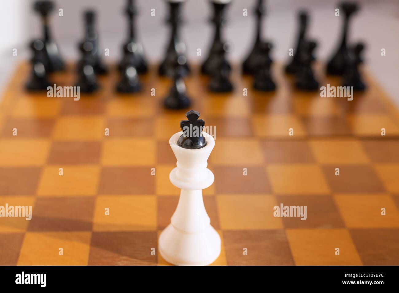 Solitario pezzo di re bianco degli scacchi si erge solo su una scacchiera di legno di fronte a un esercito nero completo sullo sfondo. Simbolo di coraggio, leadership sotto pressione Foto Stock