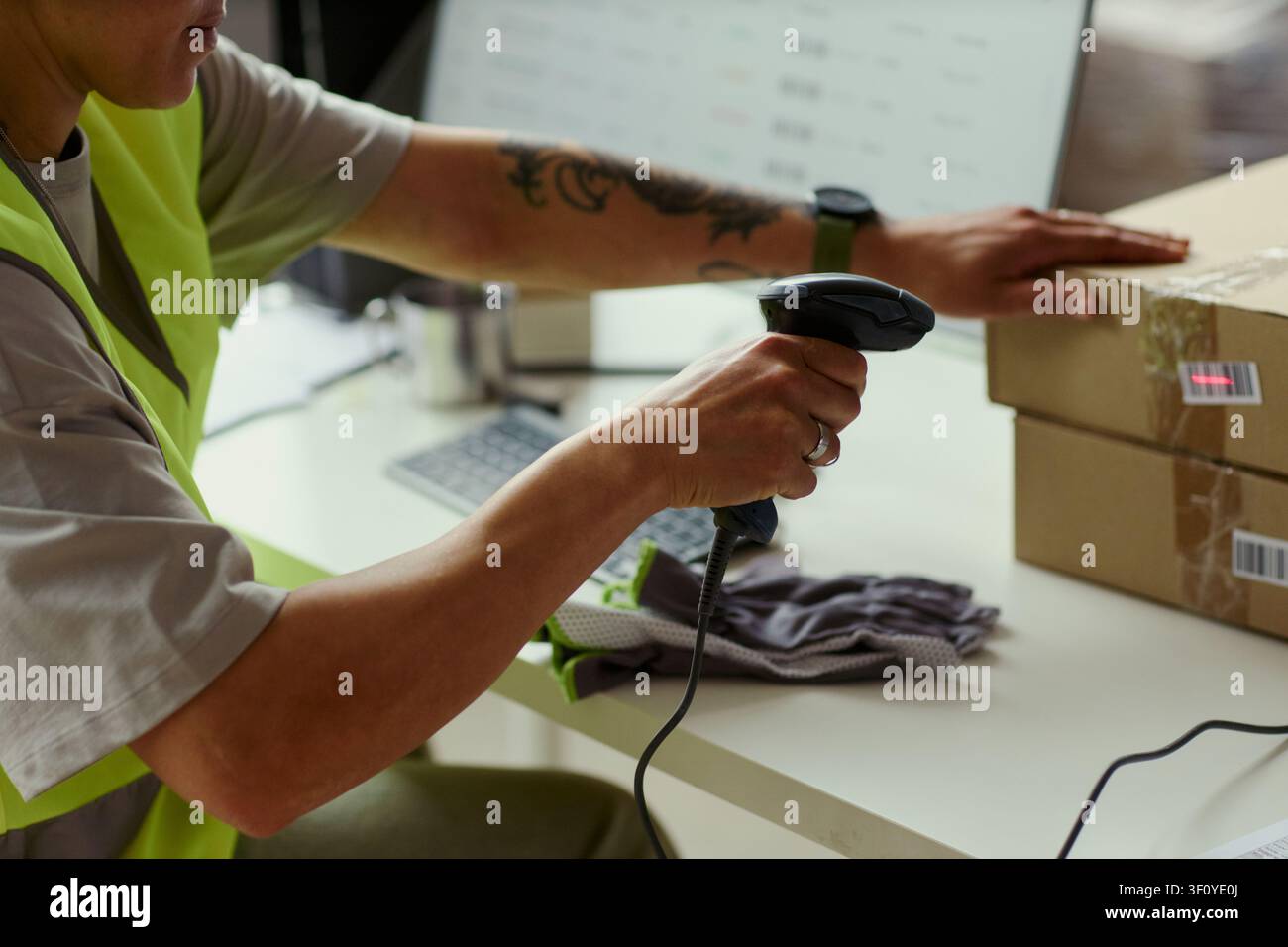 Primo piano di un giovane addetto al magazzino che scansiona un codice a barre su scatole di spedizione accanto a un computer, elaborando ordini per l'adempimento e l'inventario nell'ambito del marketing logistico del commercio elettronico Foto Stock