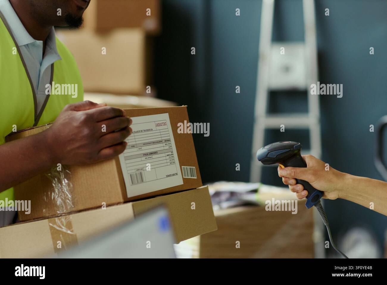 Primo piano di un addetto al magazzino di sesso maschile nero che tiene scatole di spedizione mentre un collega scansiona l'etichetta del codice a barre, supportando l'adempimento degli ordini e il marketing logistico del commercio elettronico Foto Stock
