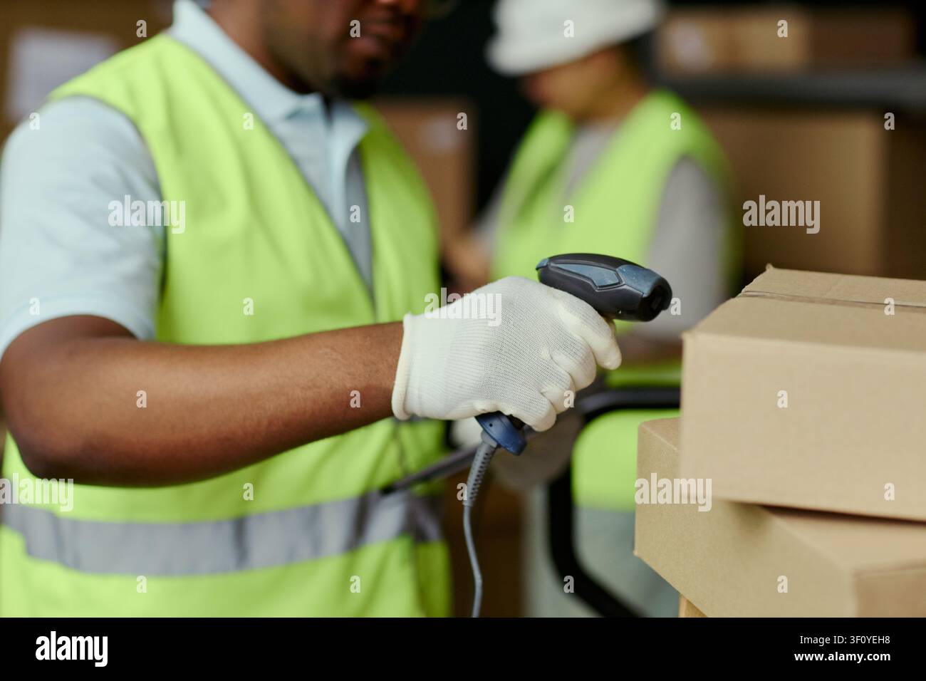 Primo piano di un magazziniere maschio di colore che scansiona cartoni con un lettore di codici a barre durante l'elaborazione dell'inventario. Utile per la logistica, l'adempimento, il marketing della catena di fornitura Foto Stock