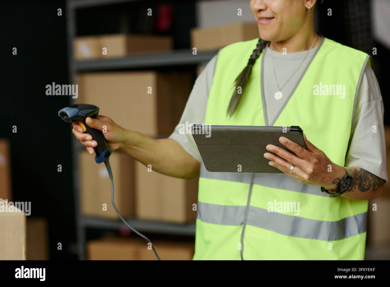 Giovane donna adulta che scansiona il codice a barre del pacco controllando il tablet nel magazzino, gestendo l'inventario e l'adempimento degli ordini. Utile per la logistica, le operazioni di vendita al dettaglio, il marketing della catena di fornitura Foto Stock