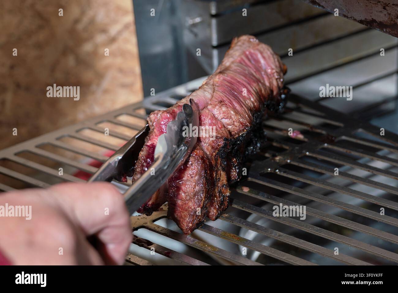 una cottura di carne in un aerogrill, bistecca a metà cottura, crosta tostata, girare un pezzo di carne sulla griglia con le pinze Foto Stock