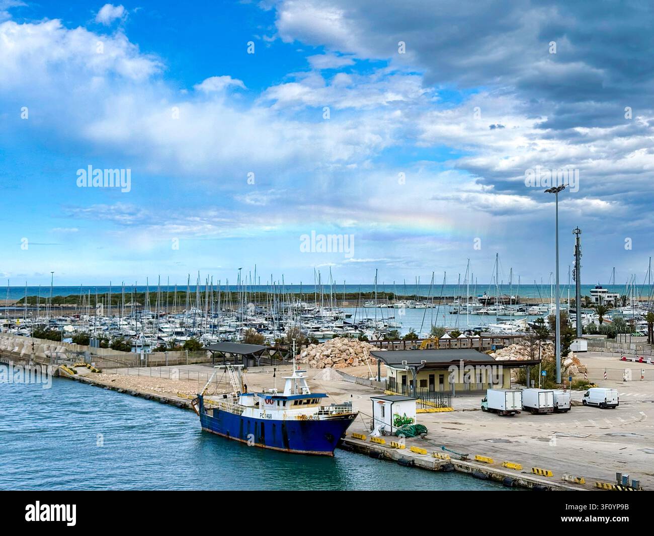 Barca da pesca blu ormeggiata sul fiume Pescara con un arcobaleno sopra la marina. Pescara, Italia - Immagine stock catturata con smartphone