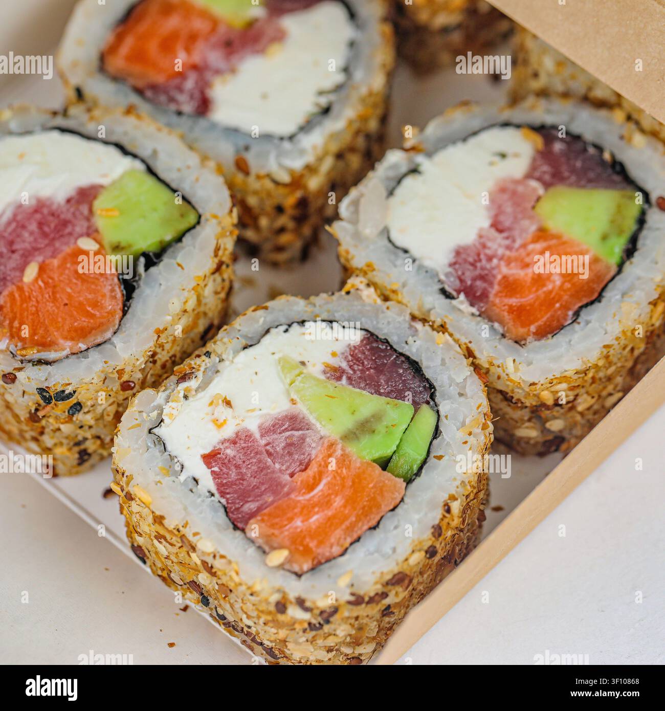 Una foto di quattro rotoli di sushi disposti ordinatamente in una scatola su un tavolo. Foto Stock